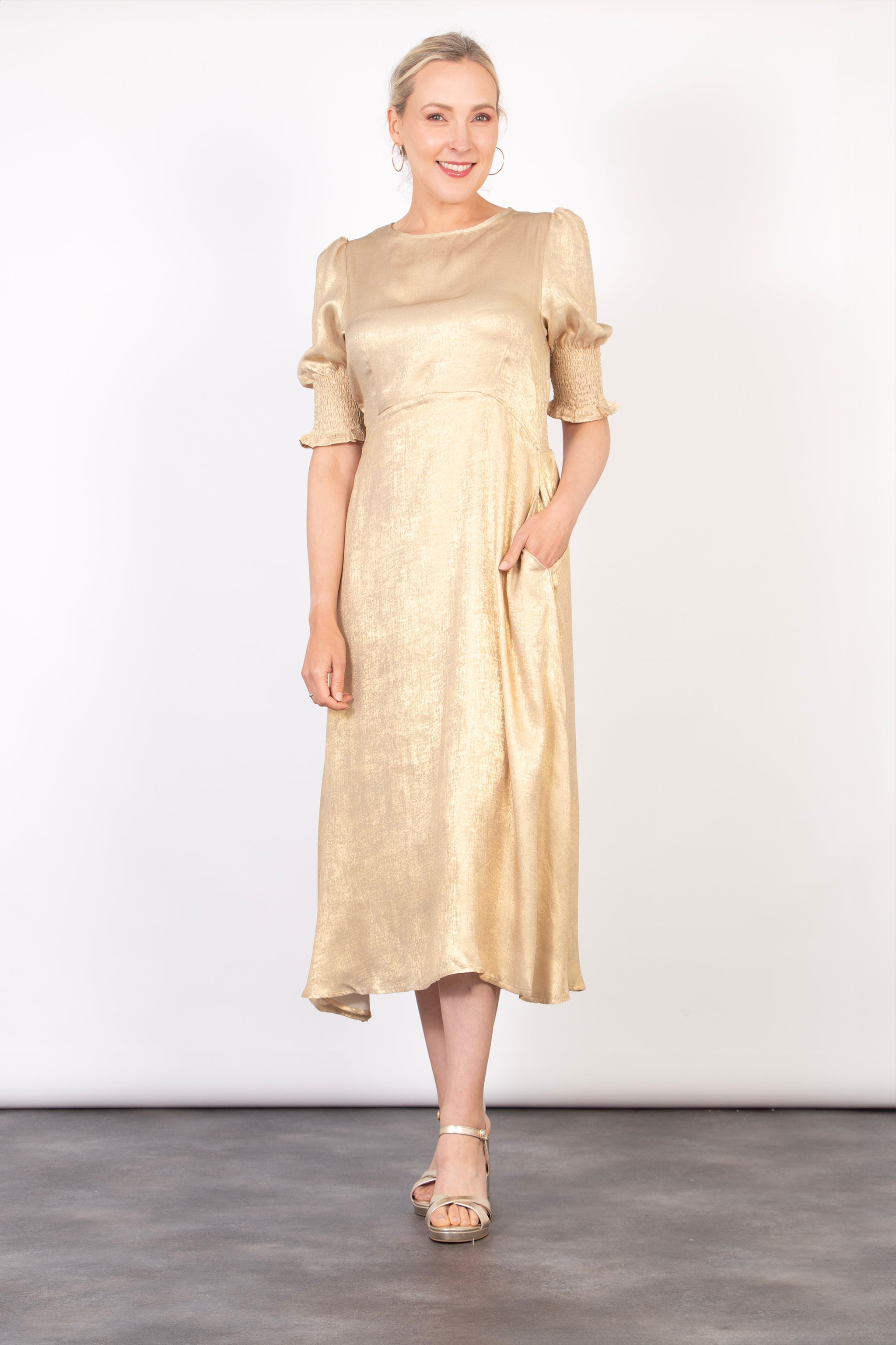 model showing that the plain gold tea dress has pockets on the front of the design