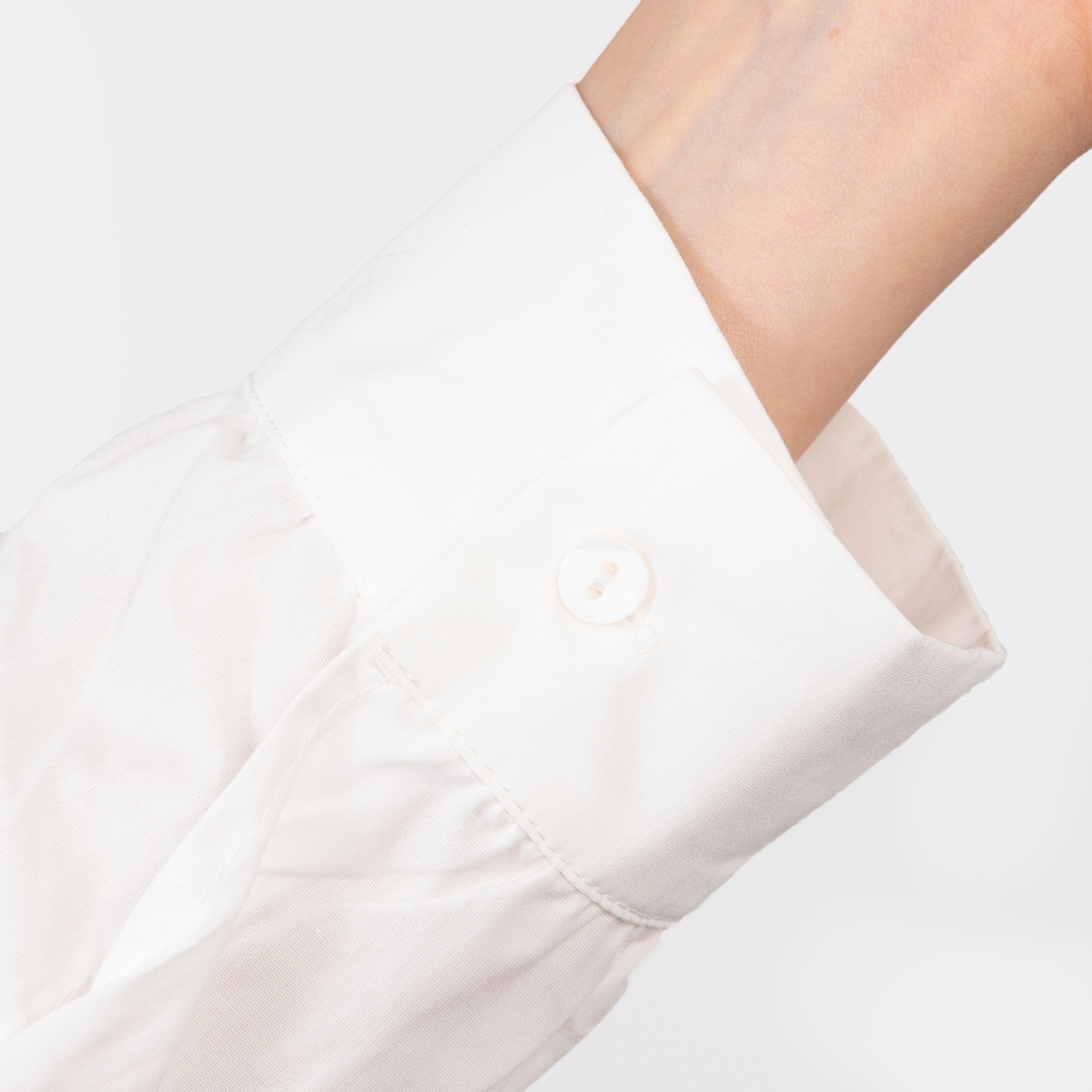 close up of the button fastening cuffs on the long sleeves of the white cotton shirt