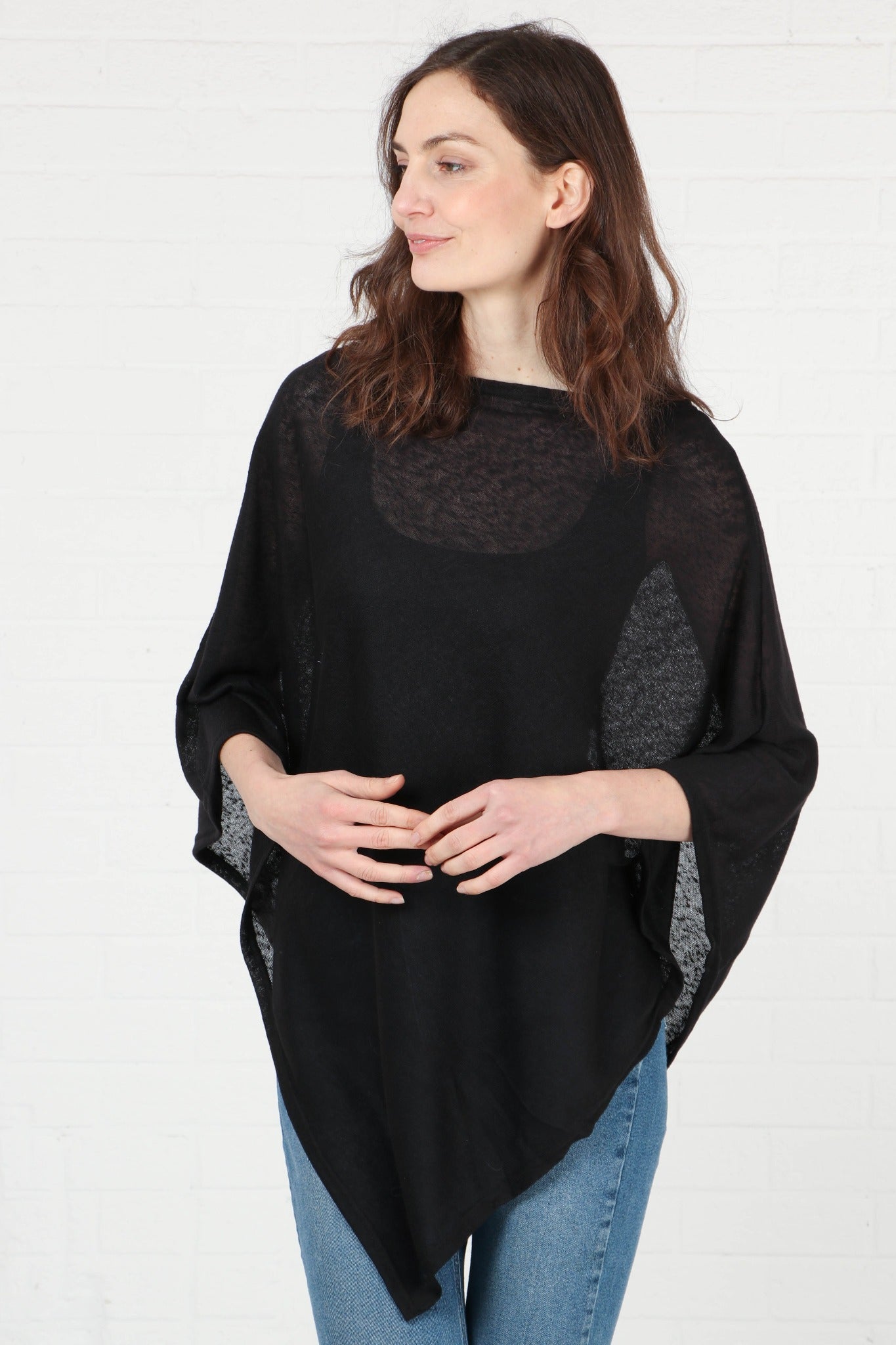model wearing the plain black poncho styled with blue jeans. the material of the poncho is lightweight and transparent