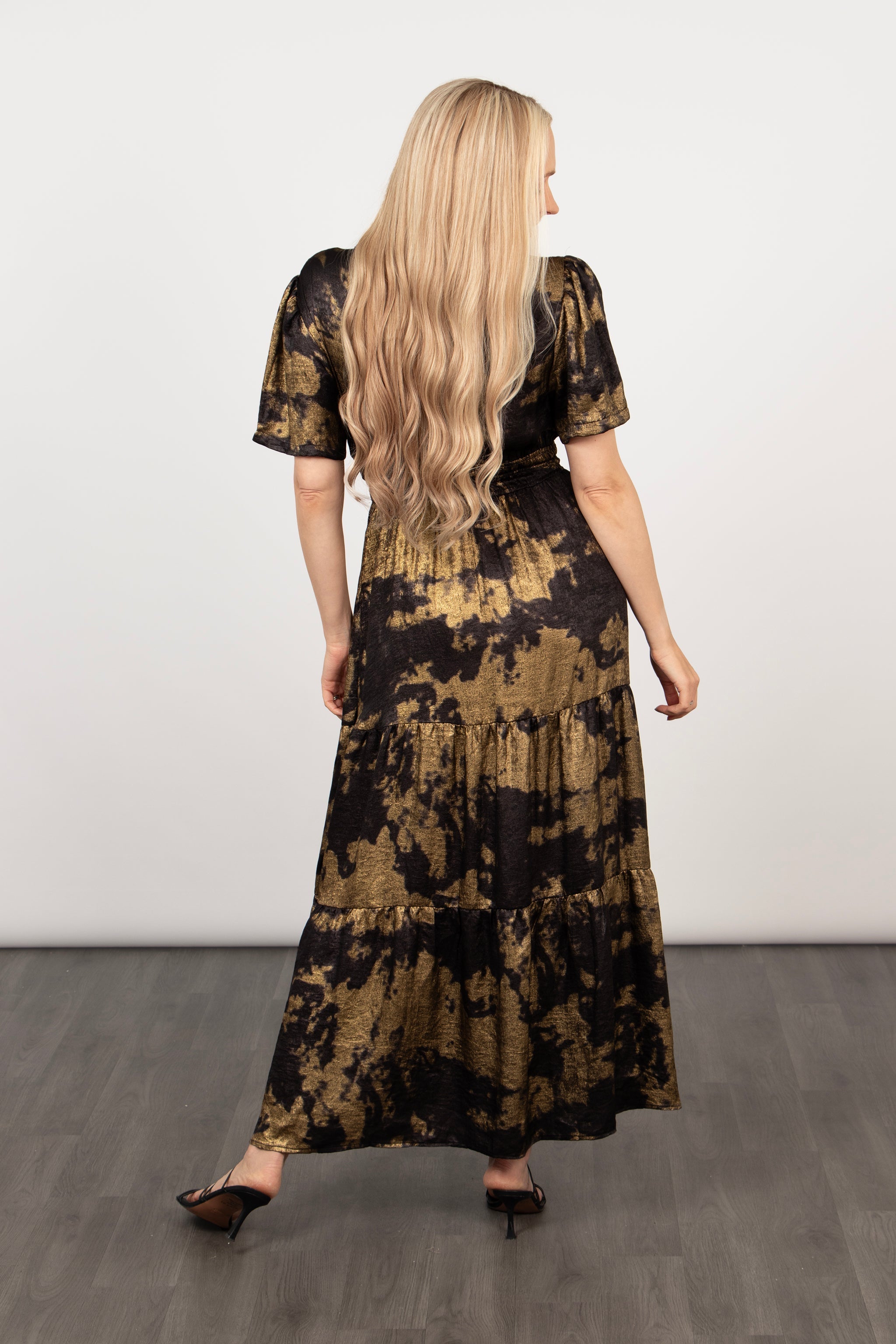 model showing the back of the tiered black and gold dress, showing the maxi length hemline