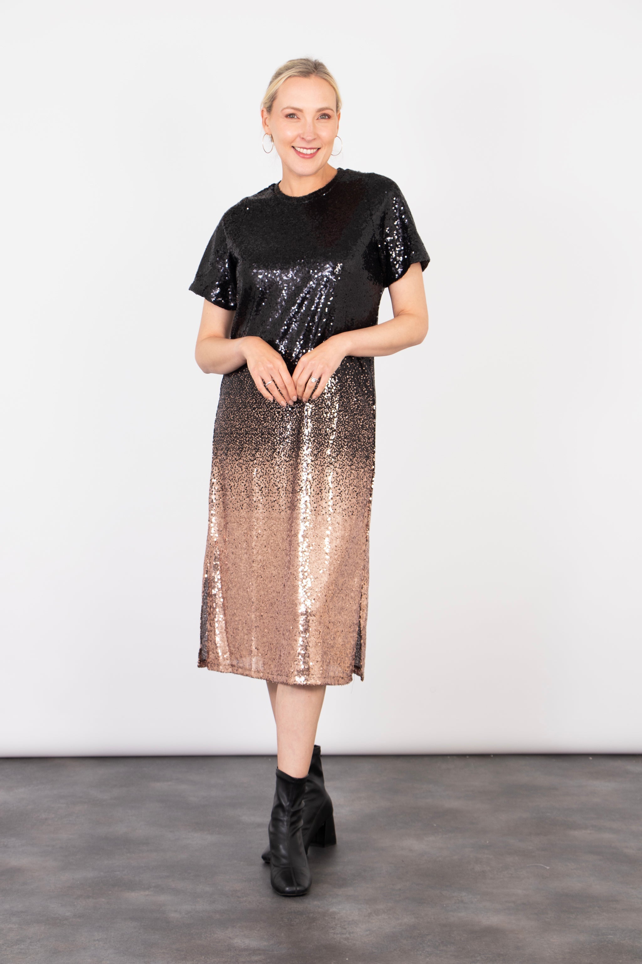 model wearing a black and bronze ombre sequin midi t-shirt dress. the dress falls just below the knee and has short sleeves and a round neck. there is an all over sequin shimmer