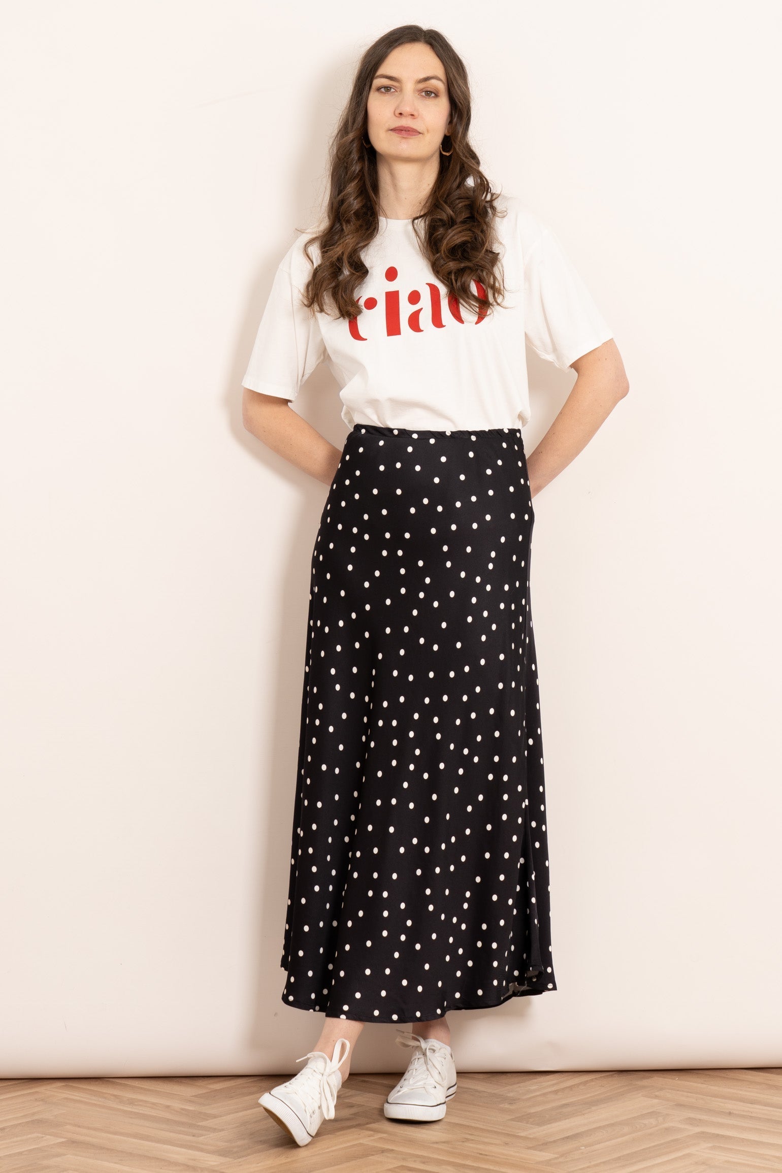 model wearing a midi length black and white polka dot print skip skirt. the skirt has an elasticated waist and is cut on the bias